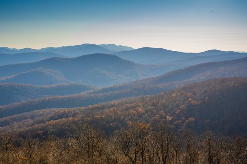 A panoramic view of rolling mountains with autumn foliage under a clear blue sky.