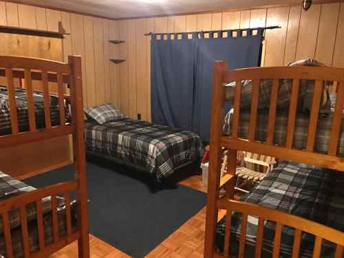 A cozy room with wooden bunk beds and single beds, featuring plaid bedding and blue curtains.