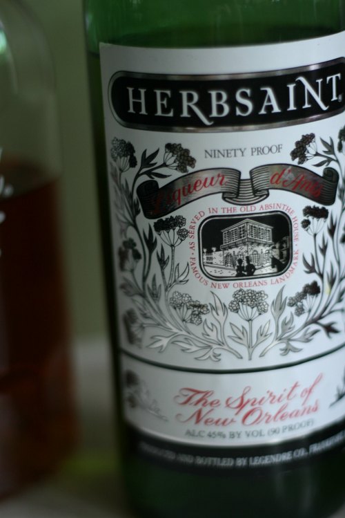 A close-up of a bottle of Herbsaint liqueur, featuring decorative label and text about its New Orleans origin.