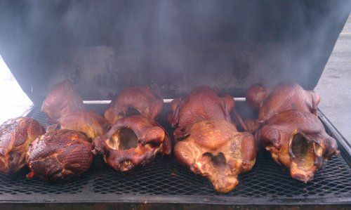 A smoker filled with several whole, smoked turkeys, emitting steam and smoke.