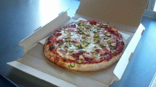 A pizza with toppings, including green peppers and ham, in an open pizza box on a table.