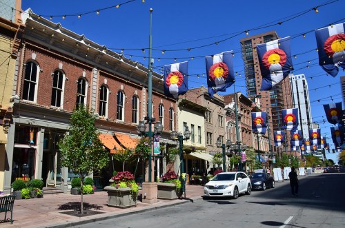 A vibrant street scene with historic buildings, colorful flags, and a white car under a clear blue sky.