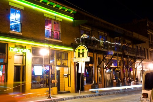 A vibrant street scene at night featuring colorful neon lights on a historic building with a bar sign.