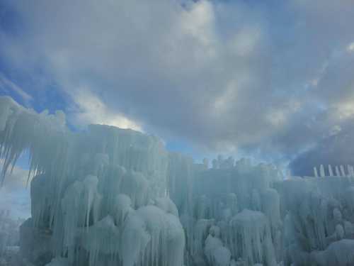 Icicles and ice formations against a backdrop of blue sky and clouds, creating a winter landscape.