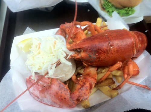 A plate of lobster with fries, lemon, and coleslaw, served in a paper tray.
