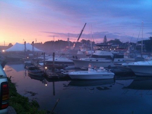 A serene marina at dawn, with boats docked and a colorful sky reflecting on the water.