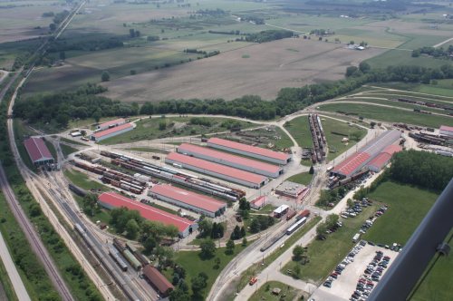 Aerial view of a train yard with multiple tracks, buildings, and surrounding farmland.