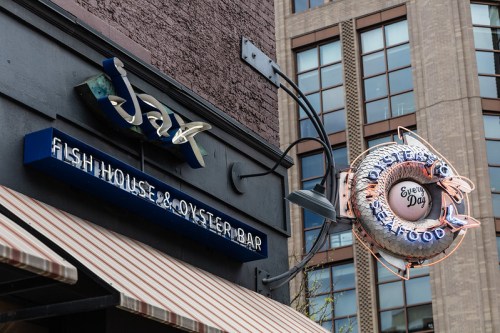 Signage for a fish house and oyster bar, featuring a neon fish and a building backdrop.