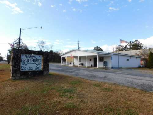 A small building with a sign reading "Welcome to Fruithurst" and an American flag, set in a rural landscape.