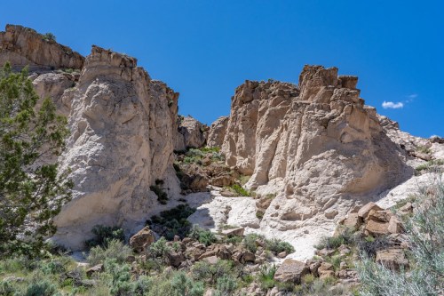 Rocky cliffs and rugged terrain under a clear blue sky, surrounded by sparse vegetation.
