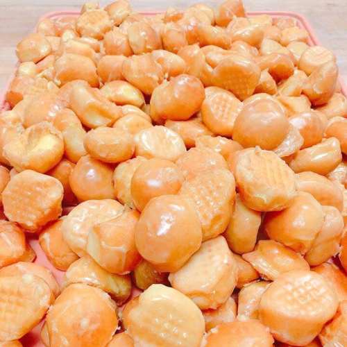 A close-up of a large pile of small, round, orange snacks with a glossy finish, arranged on a tray.