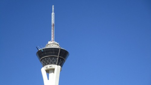 A tall observation tower against a clear blue sky, featuring a circular platform and a spire on top.
