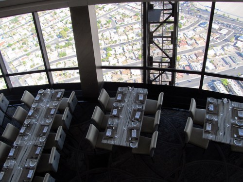 View from a high-rise restaurant overlooking a cityscape with tables set for dining.