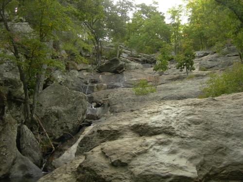 A rocky landscape with a small waterfall, surrounded by lush green trees and a serene natural setting.