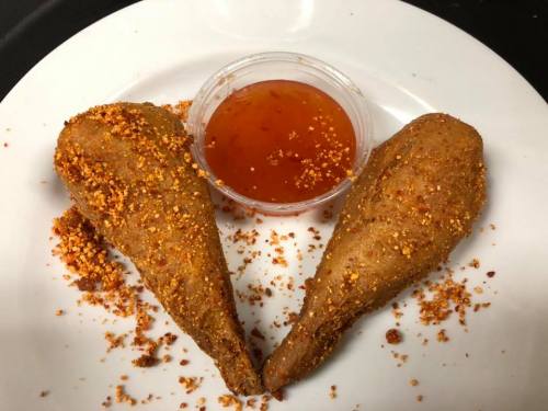 Two fried items shaped like wings, sprinkled with seasoning, served with a small cup of dipping sauce on a white plate.