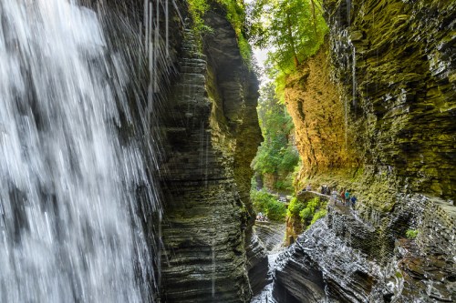 A scenic view of a waterfall cascading into a narrow gorge surrounded by towering rock walls and lush greenery.