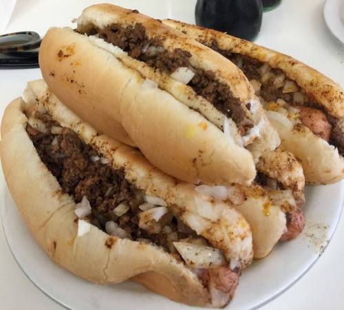 A plate stacked with hot dog buns filled with seasoned ground meat and chopped onions.