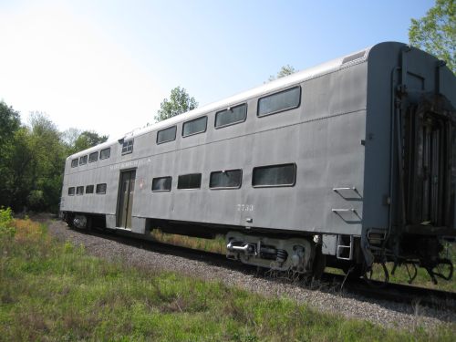 A vintage gray train car parked on a gravel track surrounded by greenery under a clear blue sky.