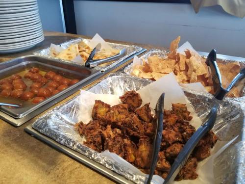 A buffet display featuring fried snacks, sweet treats, and crispy chips in metal trays lined with foil.