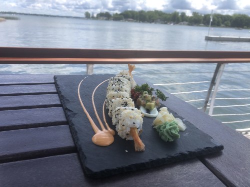 A sushi platter featuring rolls, wasabi, and garnishes, set against a scenic waterfront view.