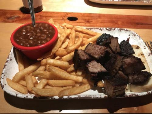 A plate of grilled meat cubes, crispy fries, and a bowl of baked beans on a wooden table.