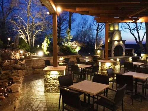 Outdoor dining area with stone tables and chairs, illuminated by soft lights, set against a twilight sky.