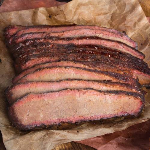 Sliced smoked brisket on parchment paper, showcasing a smoky crust and juicy pink interior.