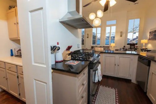 Modern kitchen with stainless steel appliances, granite countertops, and large windows, featuring a cozy living area.
