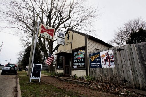 A small restaurant with a sign for Budweiser on tap, featuring a banner for Miller Lite and an American flag outside.