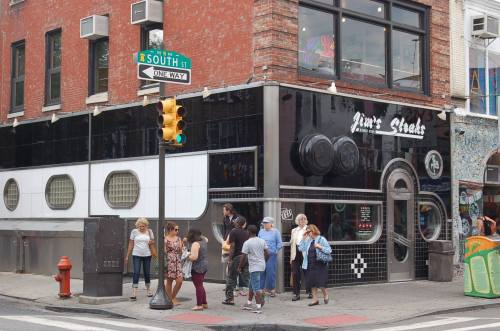 A busy street corner with people gathered outside a diner, featuring a retro-style facade and a traffic light.