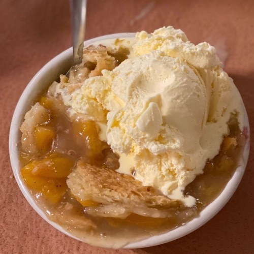 A bowl of warm peach cobbler topped with a scoop of vanilla ice cream.