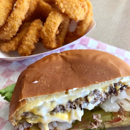 A close-up of a cheeseburger with lettuce, onions, and pickles, alongside a serving of crispy onion rings.