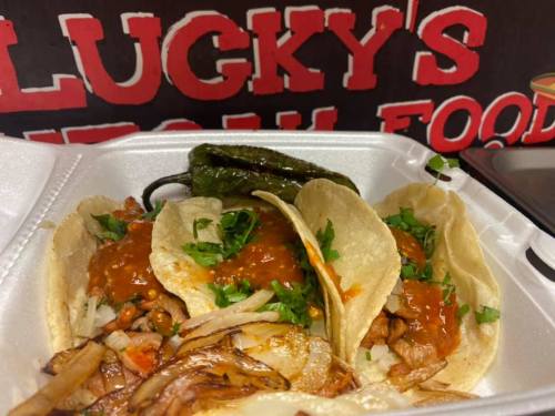 Three tacos filled with meat, topped with salsa and cilantro, served with grilled onions and a green pepper on the side.