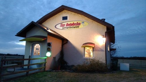 A cozy German restaurant named "Zur Autobahn" with a warm exterior, set against a twilight sky.