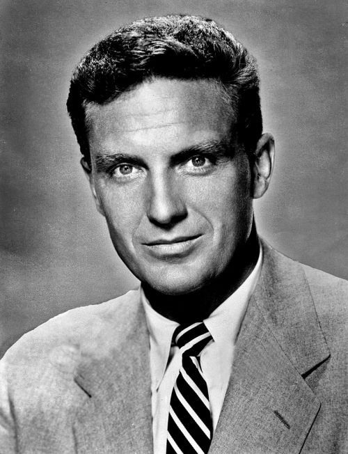 Black and white portrait of a man in a suit with a tie, smiling confidently at the camera.