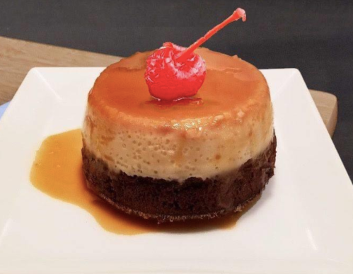 A dessert featuring a layer of flan topped with caramel and a cherry, sitting on a chocolate brownie base.