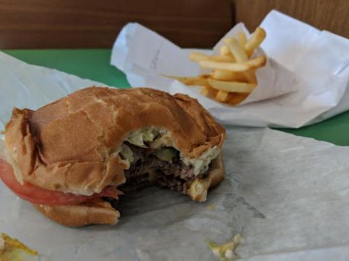 A partially eaten burger with lettuce and tomato, next to a small serving of fries in a paper bag.