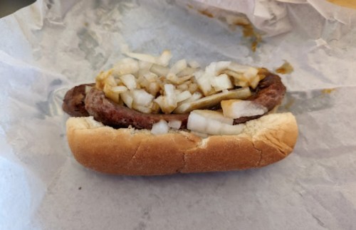 A sausage in a bun topped with chopped onions, resting on crumpled paper.