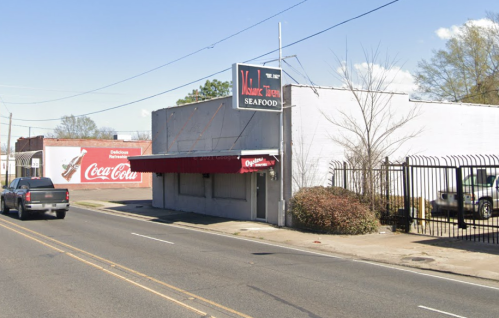 A seafood restaurant with a red awning, located on a street with a Coca-Cola advertisement on the adjacent building.