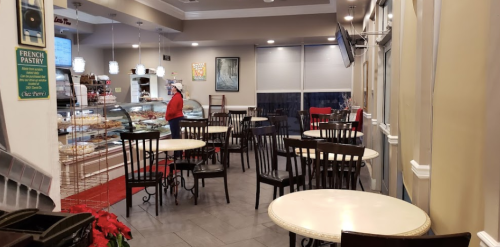 Cozy café interior with tables, chairs, and a display case of pastries; a staff member is seen in the background.