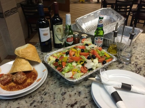 A table setting with a salad, meatballs, bread, wine bottles, and condiments on a granite surface.