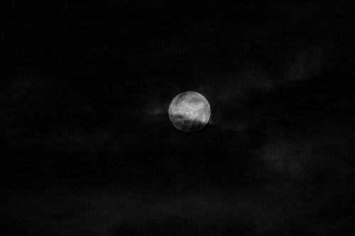 A full moon glowing softly in a dark, cloudy night sky.