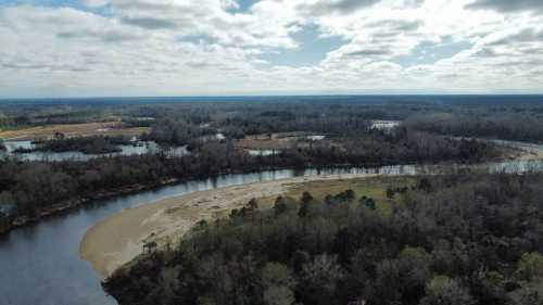 Aerial view of a winding river surrounded by lush greenery and sandy banks under a cloudy sky.