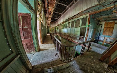 Abandoned hallway with peeling paint, broken doors, and a staircase, illuminated by green light.