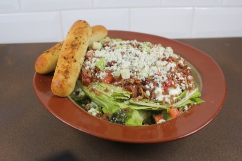 A large salad topped with bacon, cheese, and tomatoes, served with two breadsticks on the side.