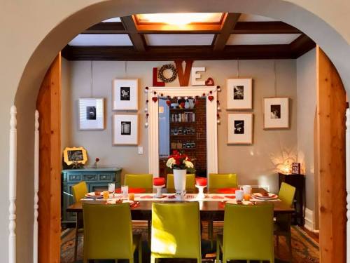 A cozy dining room with a large table set for a meal, colorful chairs, and framed photos on the walls.