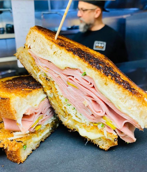 A close-up of a toasted sandwich filled with layers of ham and cheese, with a toothpick holding it together.