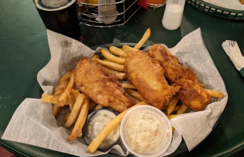 A basket of golden fried fish fillets and French fries, served with coleslaw and dipping sauce.