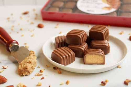 A plate of chocolate-covered candies with a creamy filling, surrounded by chopped almonds and a knife with spread.