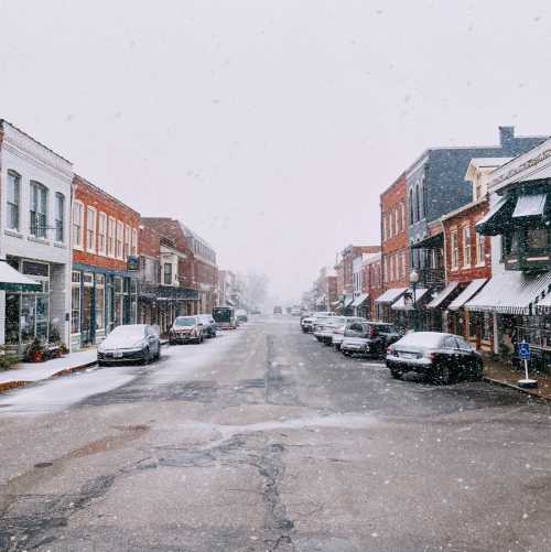 A snowy street scene with historic buildings and parked cars, creating a quiet, winter atmosphere.